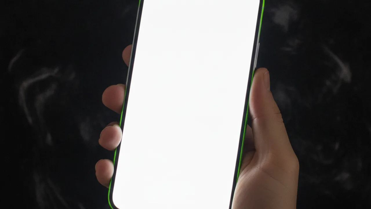 Karanlık zeminde boş parlak ekranlı telefonu tutan el, kenarında lime yeşili ışık